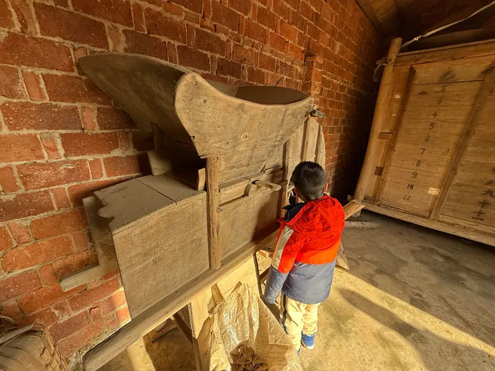 A child beside a wooden farm tool inside a brick building.