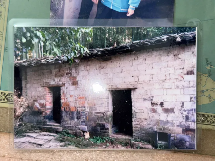 A photograph of an older printed image of a house, showing a window and an open doorway.