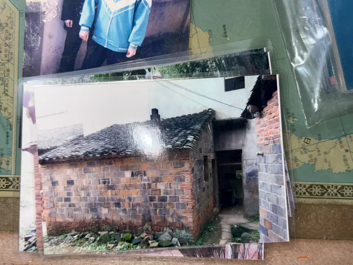 A photograph of an older printed image of a brick house with a tiled roof and an open doorway on the right.