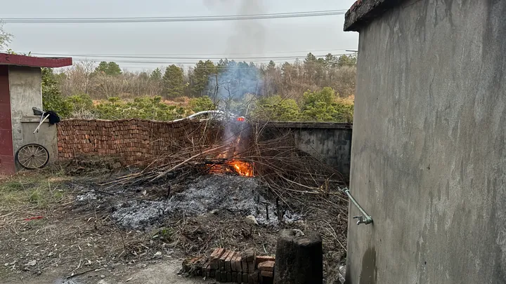 Smoke rising from burning branches beside a wall.