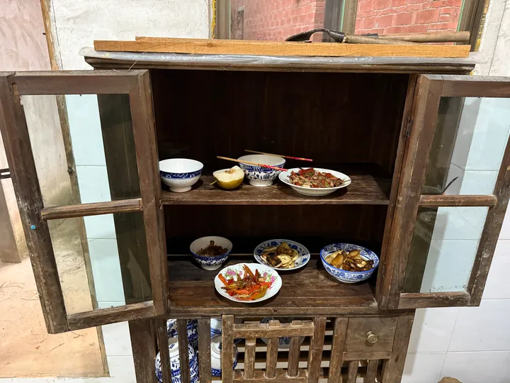 Bowls, chopsticks, and dishes of food inside a wooden cupboard.
