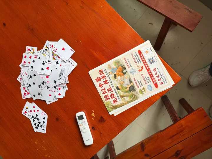 Playing cards, a remote control, and YiLao WeatherLink leaflets on a wooden table.