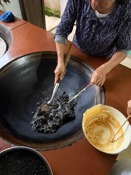 Food being stirred in a large wok, beside a bowl of pale yellow mixture.