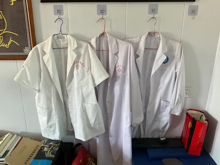 Three white medical coats hanging side by side on a wall.