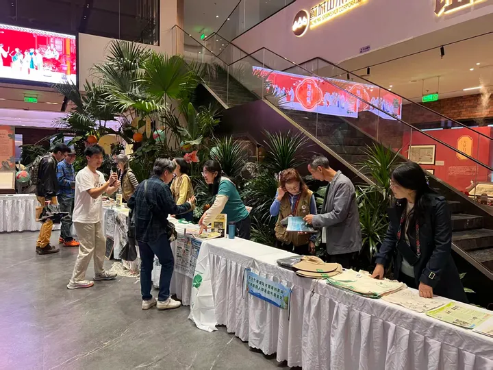 Visitors reading and discussing materials at long tables inside a public event.