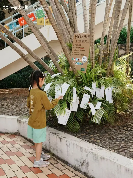 A child reading question cards suspended beside a tree.