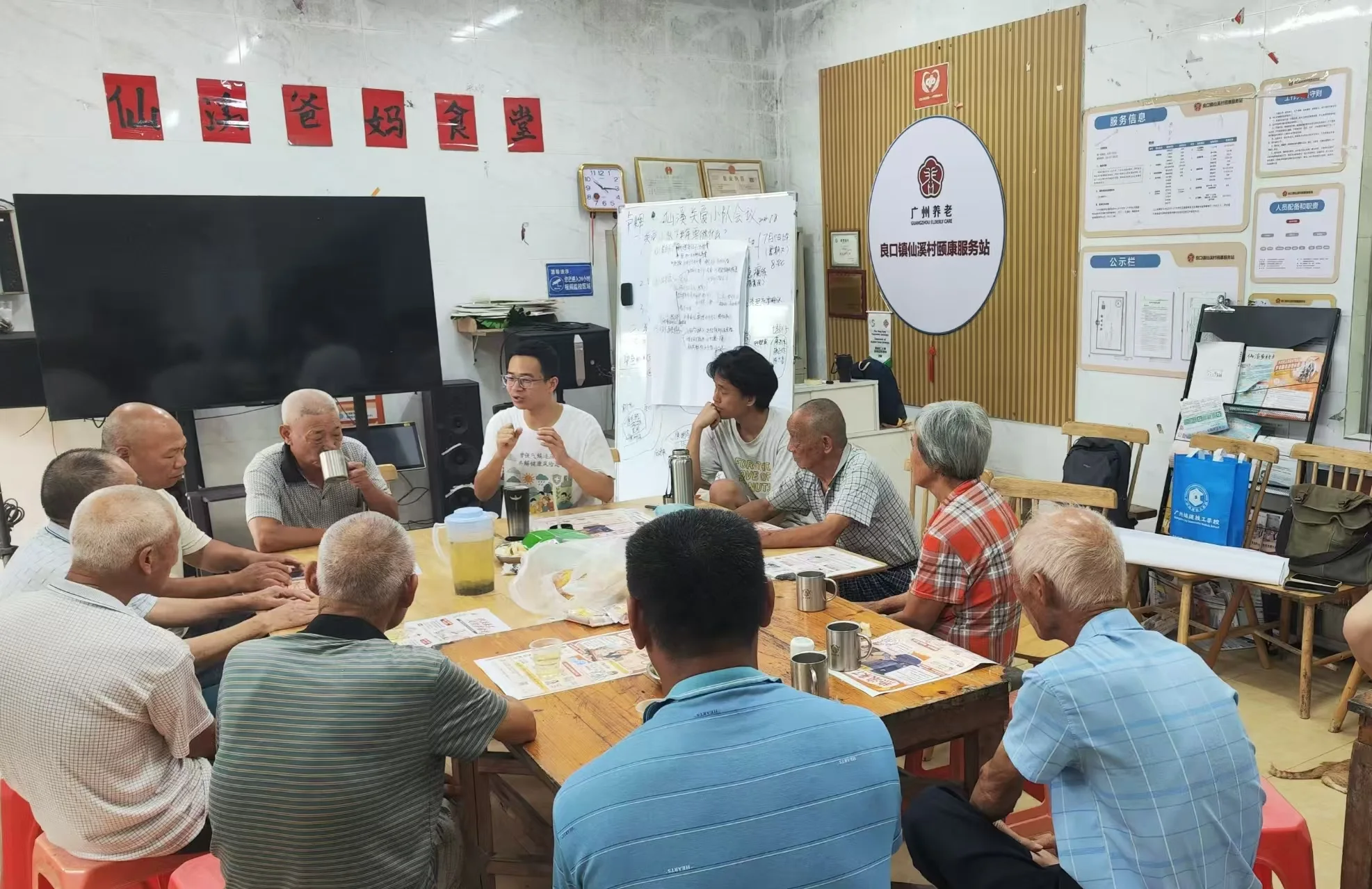 Older adults and other participants talking around a table with printed materials.