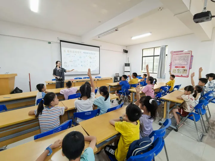 A presenter interacting with children raising their hands in a classroom.