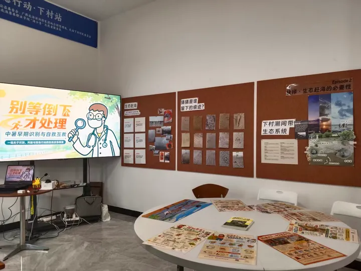 Printed materials arranged on a round table beside a screen showing a heat-awareness topic.